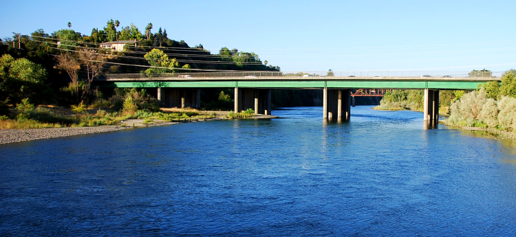Photo of the American River with an overpass and bridge in the background