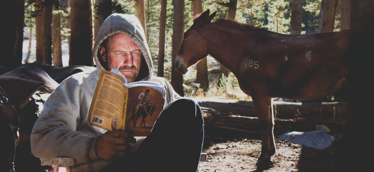 Chris Culcasi reading a book in front of his horse
