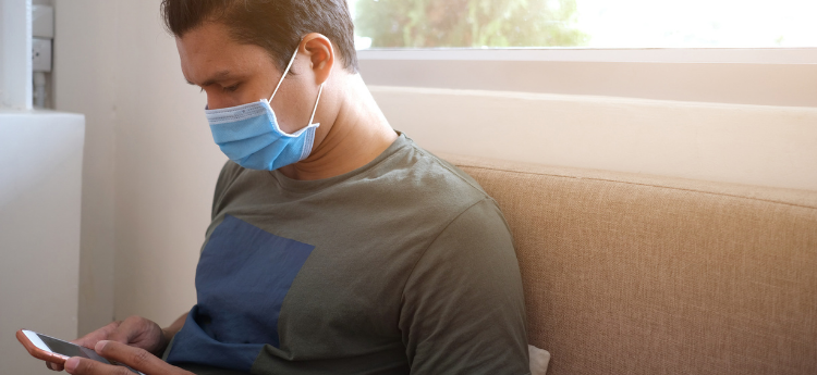Hispanic male sitting on a couch and wearing a surgical mask 