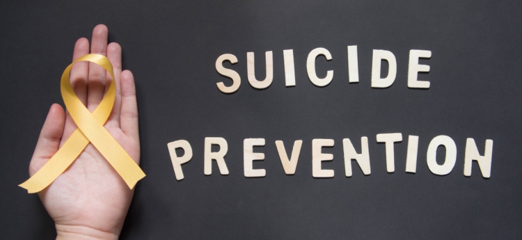 Hand holding a yellow ribbon with text that reads "Suicide Prevention" 