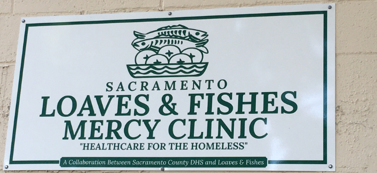 White sign on brick wall that reads "Sacramento Loaves and Fishes Mercy Clinic  'Healthcare for the Homeless'" 